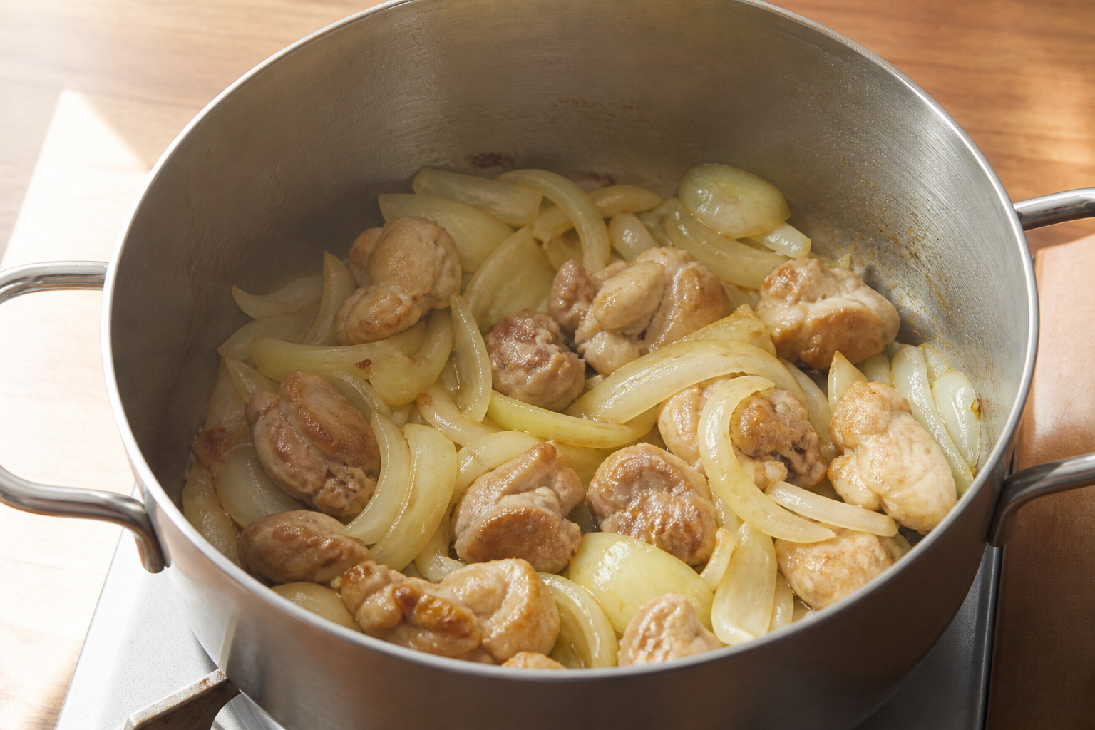Sliced onions softening with browned chicken in a cooking pot