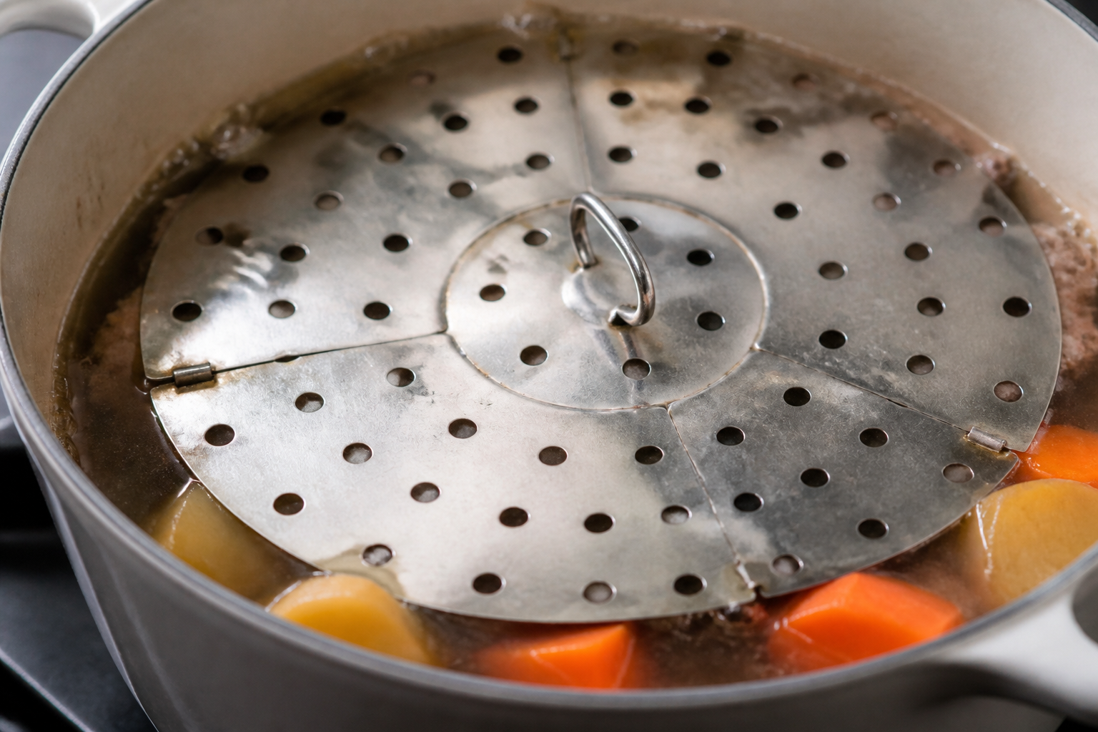 Nikujaga simmering under a perforated drop lid in a saucepan